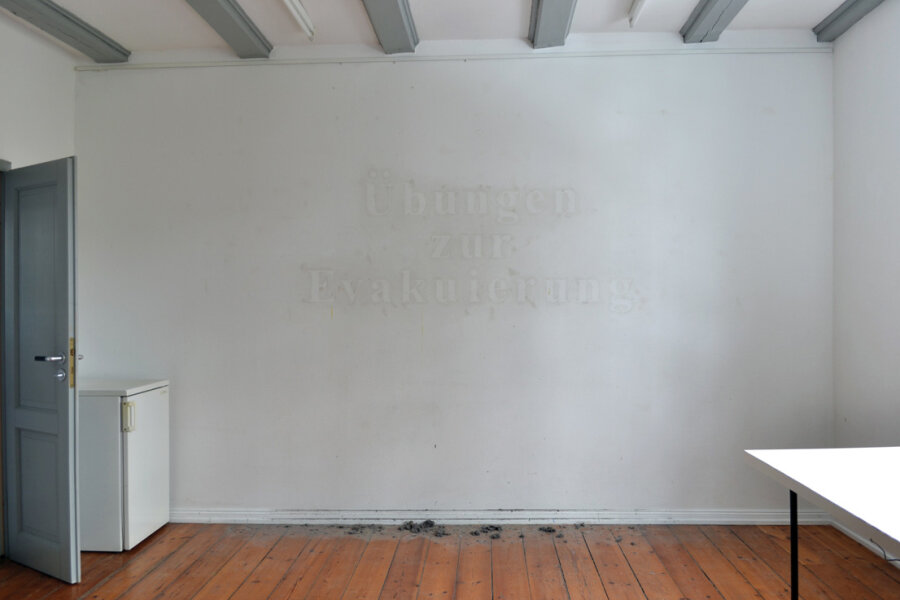 “Übungen zur Evakuierung / Evacuation drills” (from the series “Fallout shelters and dictionaries”) – inscription in dust on an empty wall / Ahrenshoop / Germany / 2013